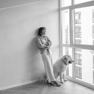 caucasian woman standing in an empty apartment with her dog looking out the window
