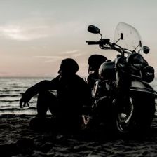 a man sitting on a beach with his motorcycle