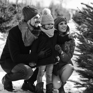 B&W image of a mother and father with their young daughter picking our a christmas tree
