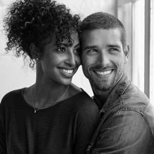 An interracial couple smiling and sitting next to a window