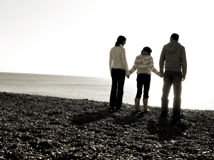 a family of three standing near the beach